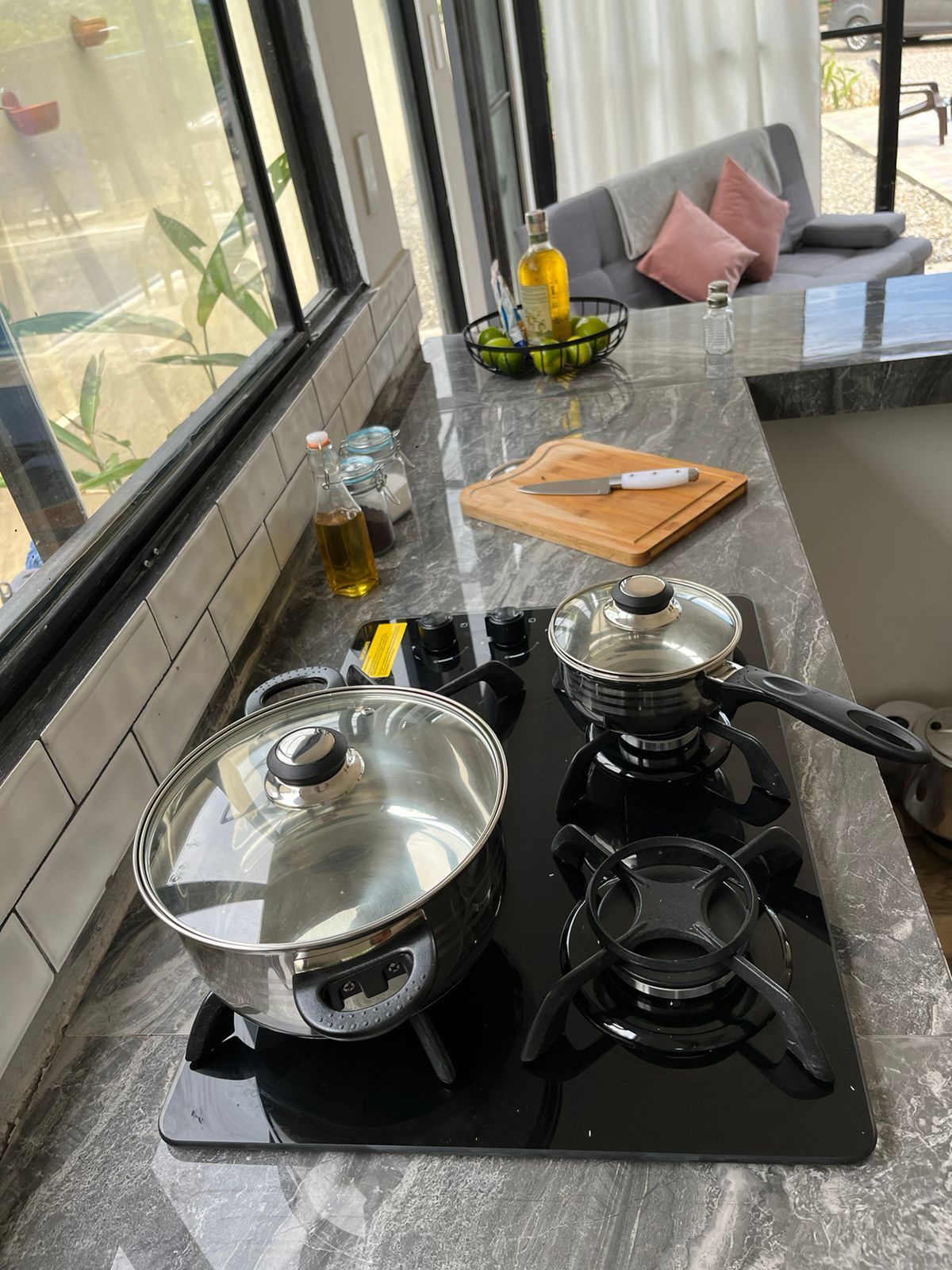 Una cocina con estufa a gas, una olla sobre la hornilla izquierda, tabla de cortar con cuchillo y un cuenco de fruta en la encimera.