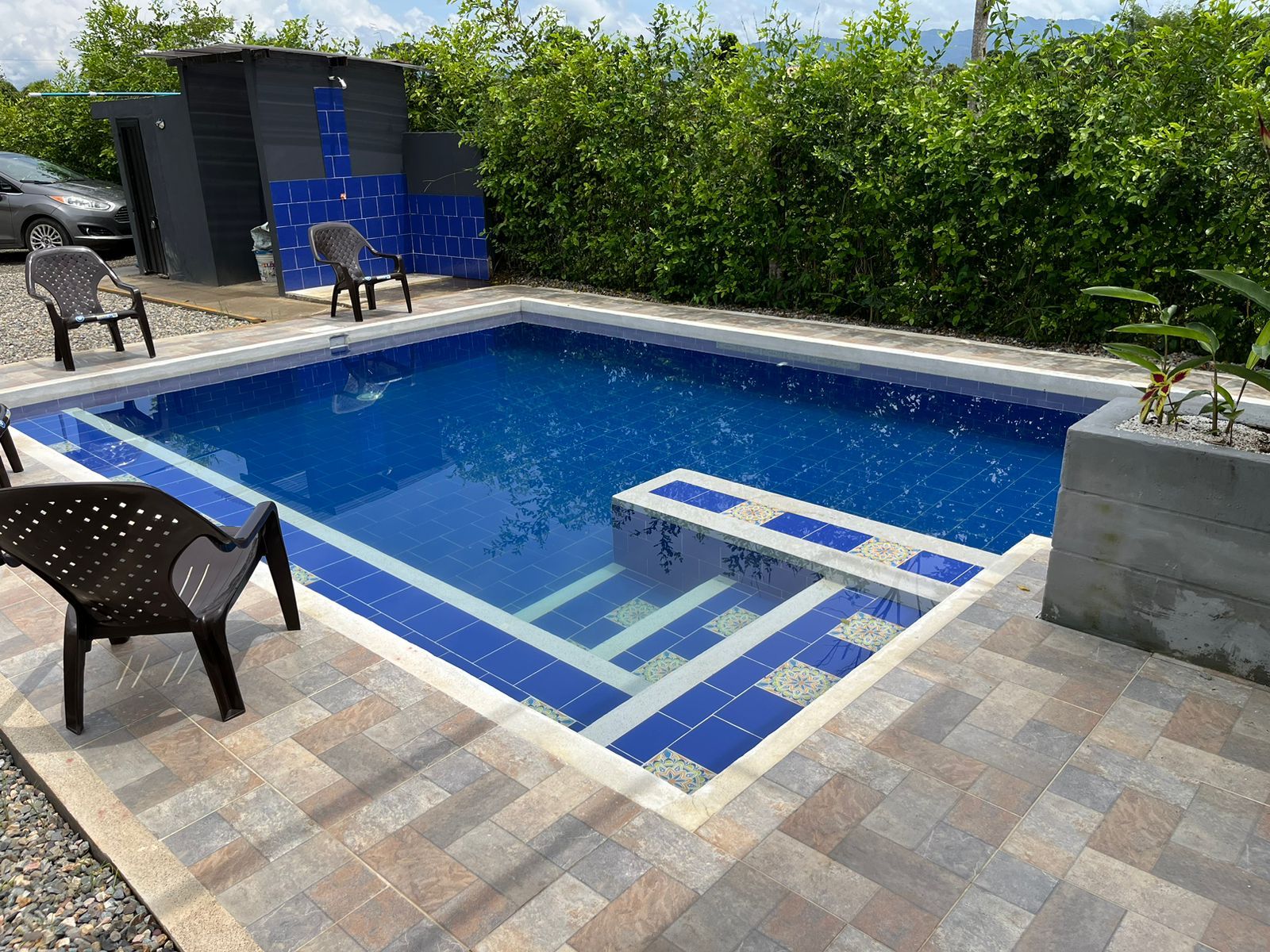 Et rektangulært pool med blå fliser og en flisebelagt terrasse.