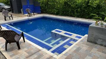 Et rektangulært pool med blå fliser og en flisebelagt terrasse.