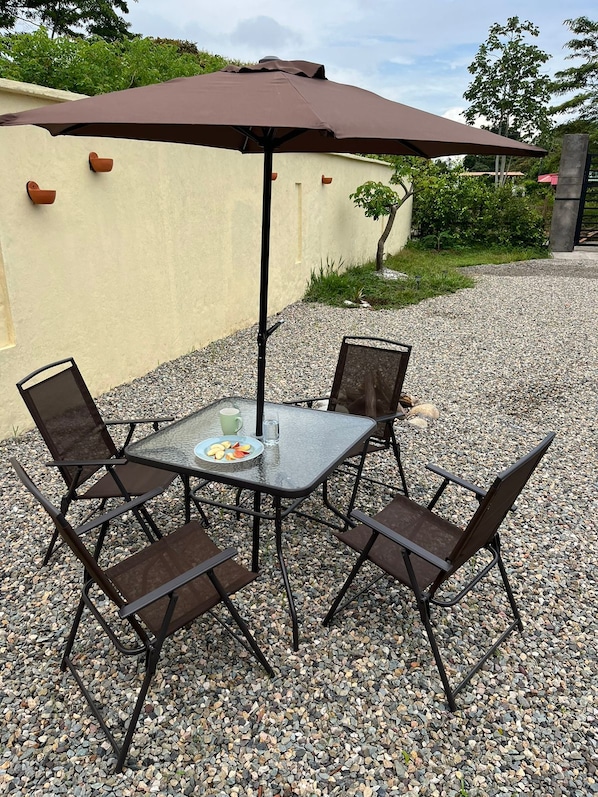 An outdoor patio with a table and four chairs, an umbrella, and a small plate of fruit.
