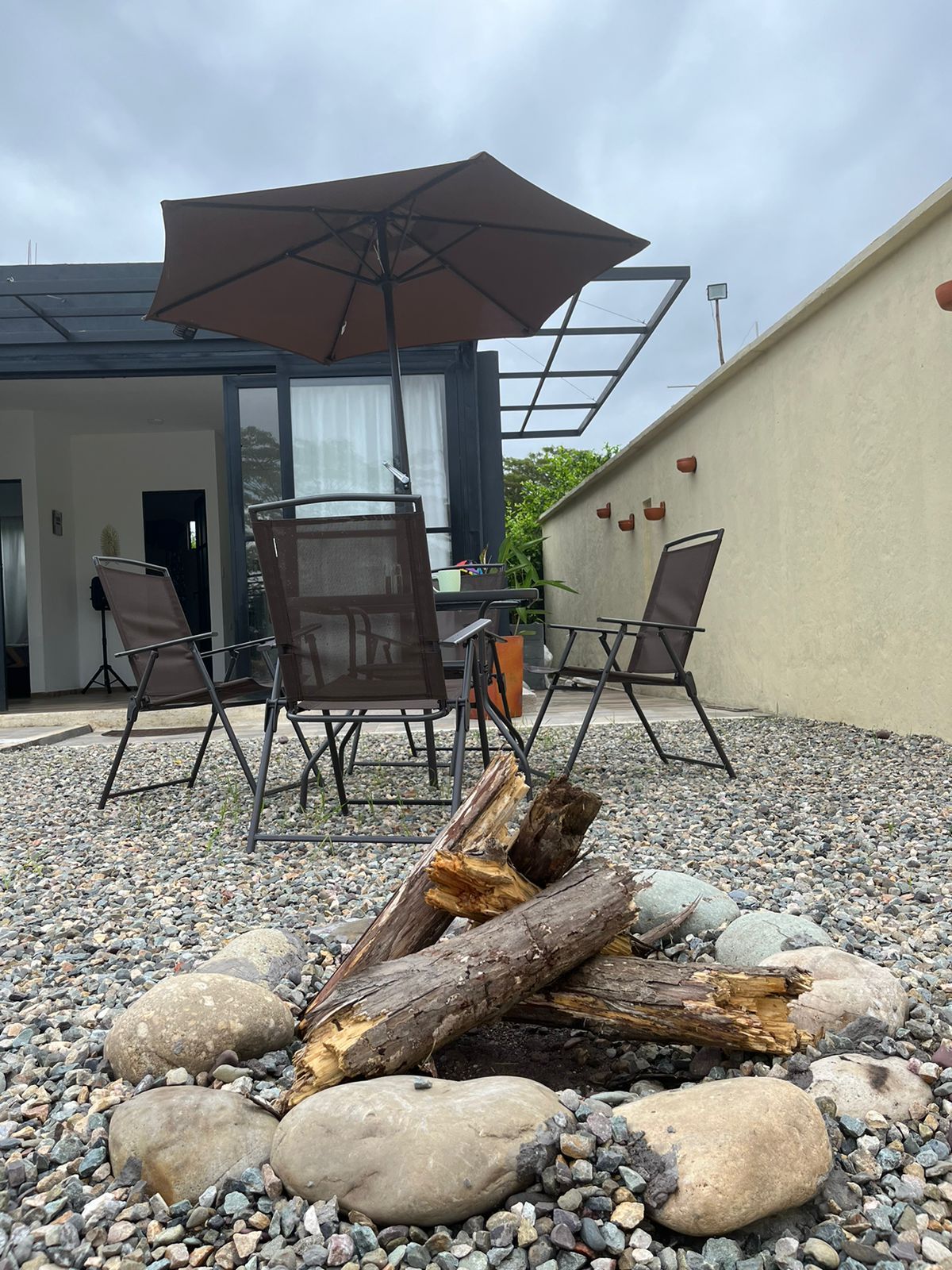 Un área de estar al aire libre con una mesa, sillas y una chimenea rodeada de guijarros.