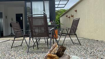 Un área de estar al aire libre con una mesa, sillas y una chimenea rodeada de guijarros.
