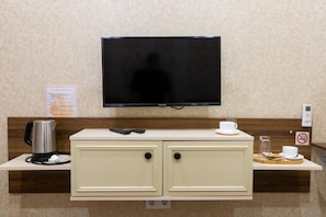 A hotel room with a flat-screen TV mounted above a cream-colored minibar, a kettle, and a cup on the counter. - Midcity Hotel (Baku)