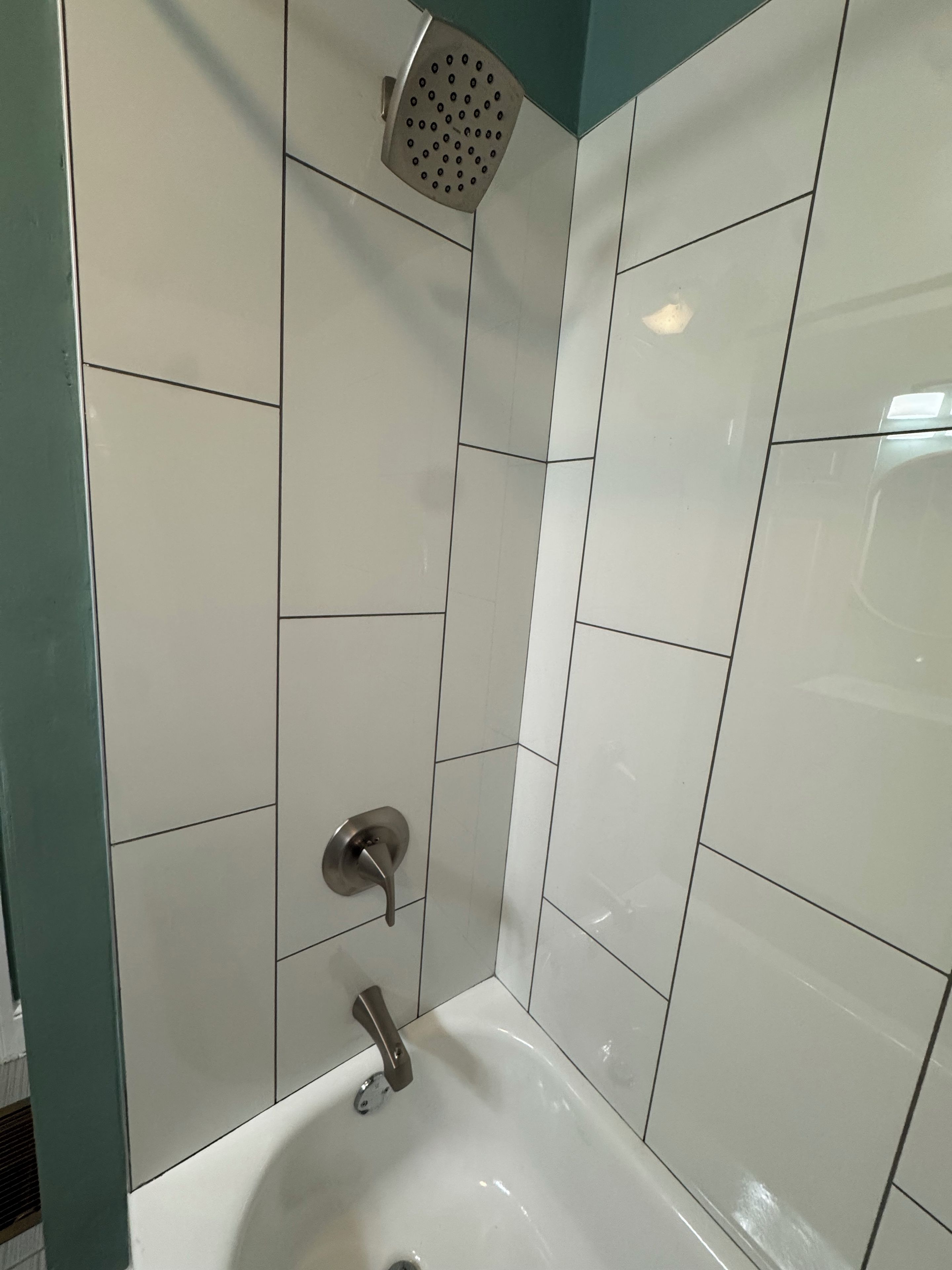 Baño con azulejos blancos, un cabezal de ducha y un lavabo.