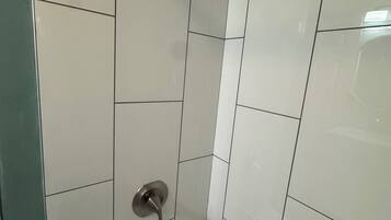 Baño con azulejos blancos, un cabezal de ducha y un lavabo.