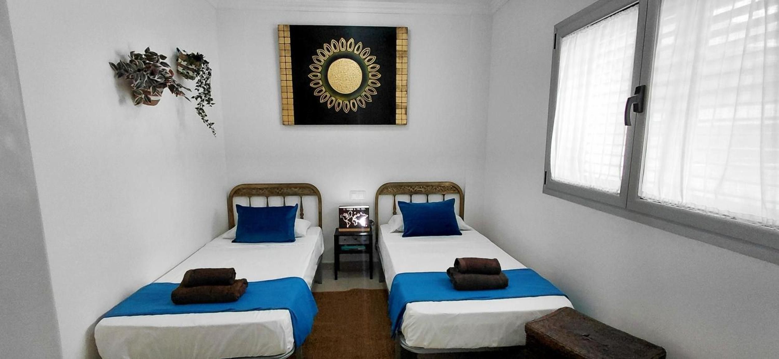 Habitació petita i senzilla amb dos llits individuals, una finestra i un mirall decoratiu penjat a la paret.