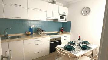 Een kleine keuken met witte kastjes, een magnetron, een spoelbak en een eethoek met een tafel gedekt voor twee personen.