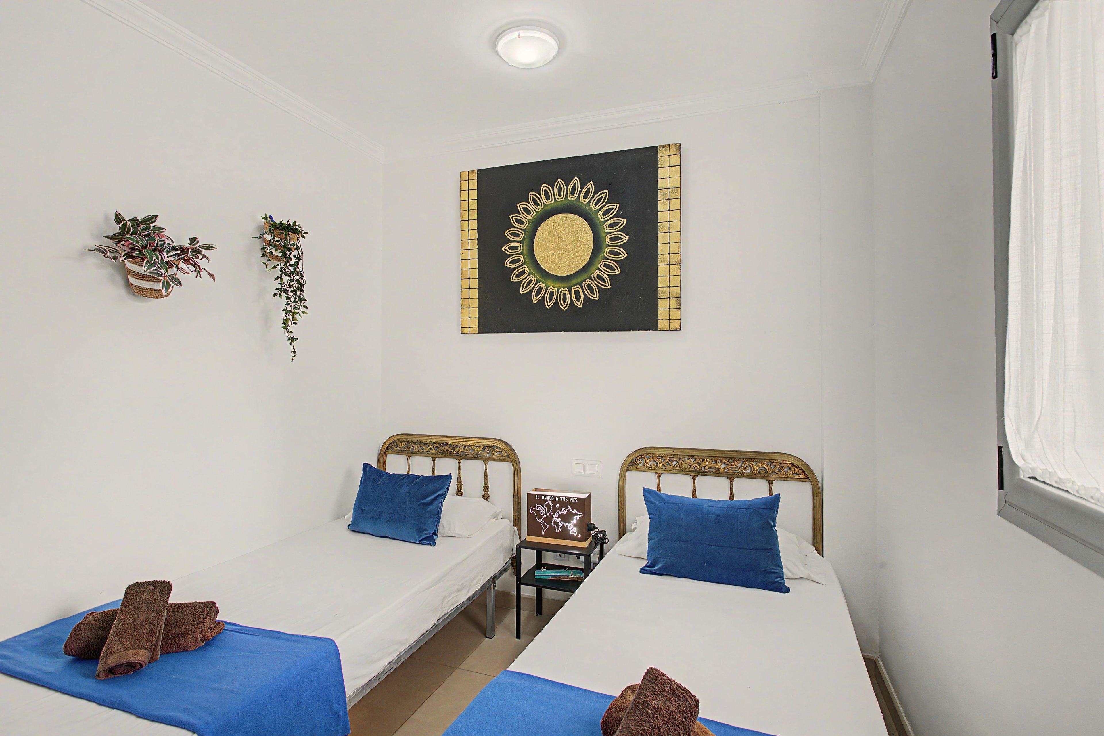 Una habitación con dos camas individuales, un adorno en la pared y una mesita con un libro.
