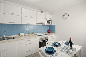 A modern kitchen with white cabinets, a blue tiled backsplash, a built-in microwave, and a dining area with a table set for two.
