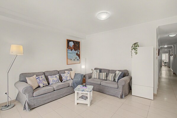 A living room with a grey sofa set, a white coffee table, a floor lamp, a painting on the wall, and a plant on the wall.