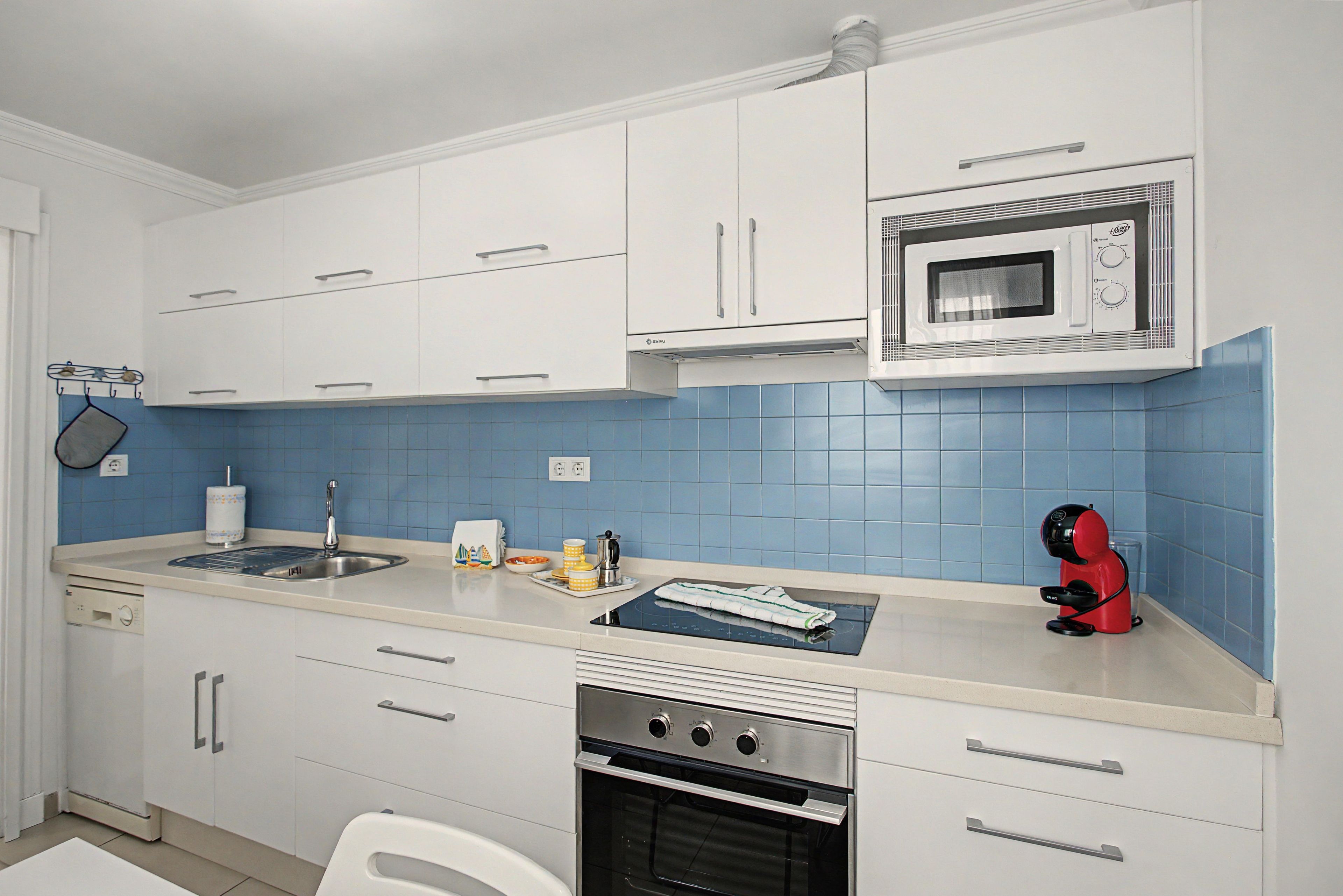 A compact kitchen with white cabinets, a built-in microwave, a stove, and a sink.