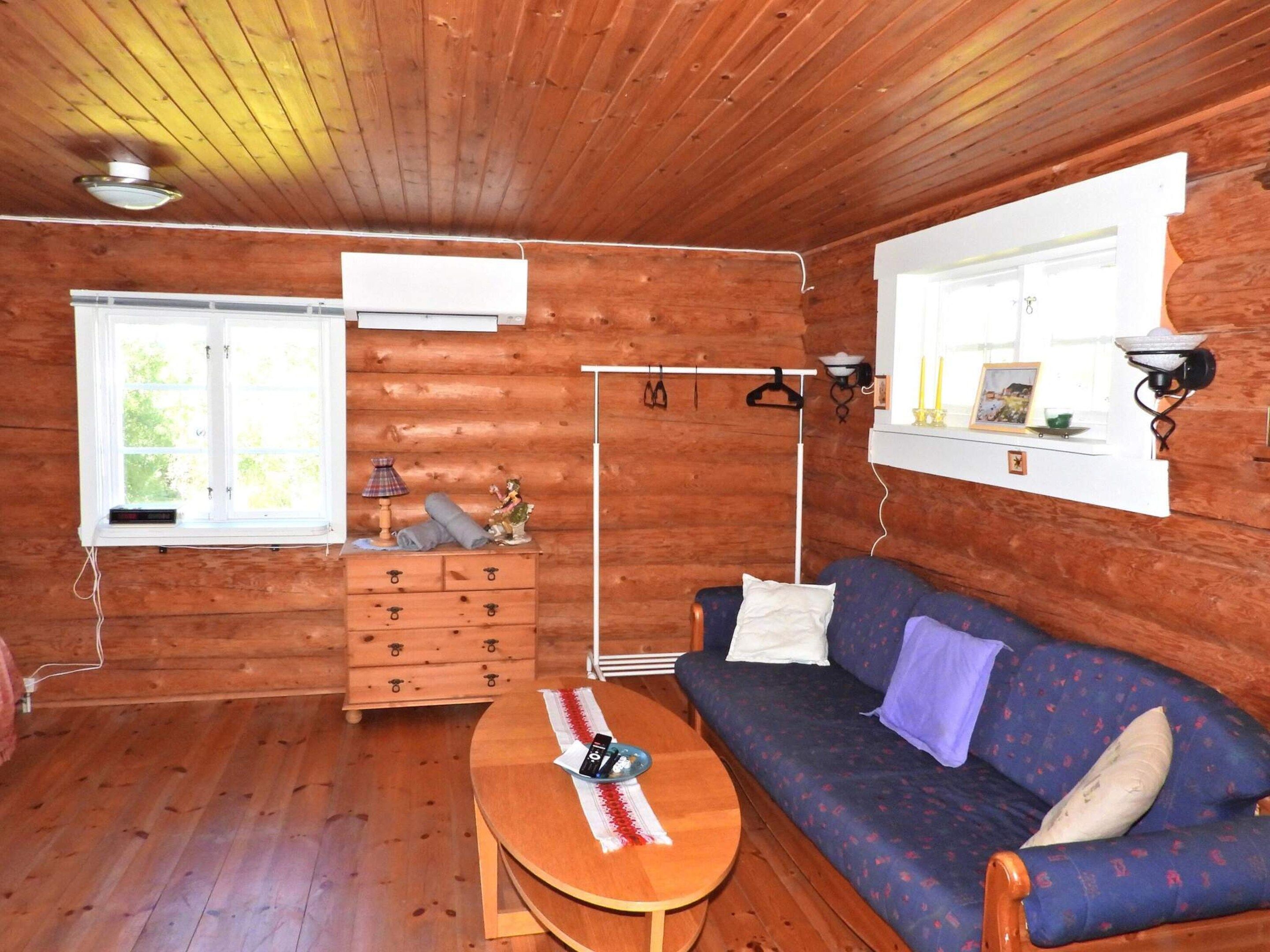 A cozy cabin interior with a wooden floor, a sofa, a table, a dresser, and a window with a view.