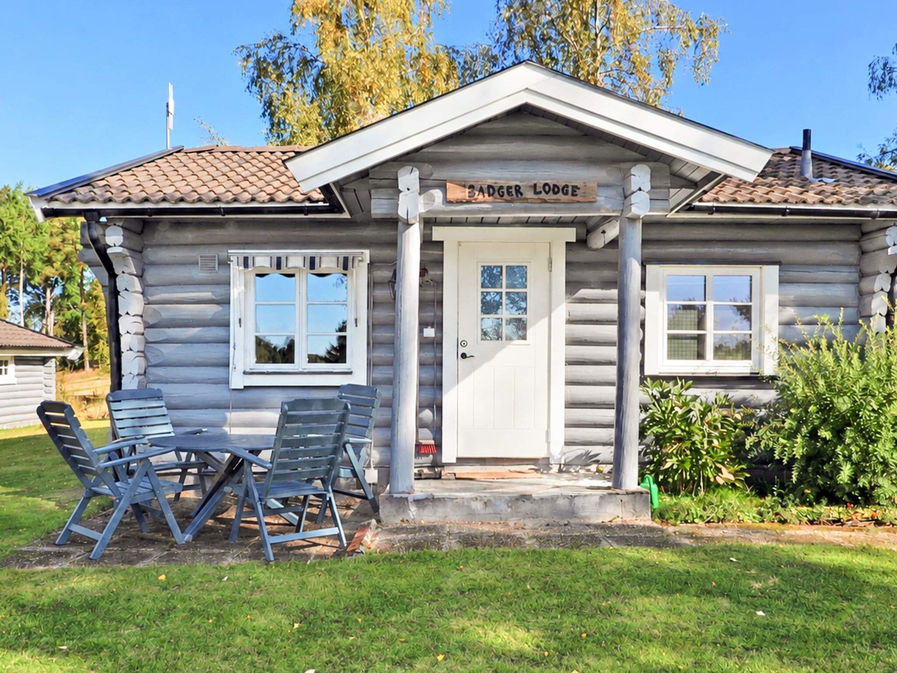 A log cabin with a sign reading 'Badger Lodge' and two folding chairs outside.