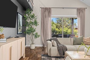 Una sala de estar moderna con un sofá, una mesa de centro, una planta en maceta y un gran ventanal con cortinas.