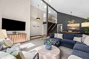 A modern living room with a sectional sofa, a flat-screen TV, a wooden coffee table, and a staircase leading to an upper level. - Waterfront-Gym-Patio-Pool Table (Boise)