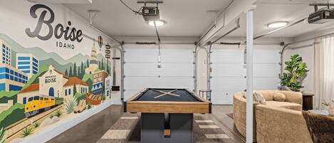 Una mesa de billar en una habitación con un mural de Boise, Idaho, un sofá y una planta.