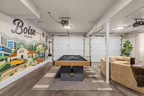 A pool table in a room with a mural of Boise, Idaho, a couch, and a plant. - Waterfront-Gym-Patio-Pool Table (Boise)