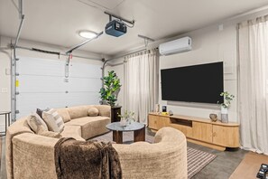 A modern living room with a sectional sofa, a coffee table, a flat-screen TV, and a ceiling-mounted projector. - Waterfront-Gym-Patio-Pool Table (Boise)