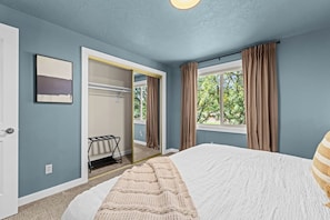 A bedroom with a large bed, a window with curtains, a door, and a coat rack. - Waterfront-Gym-Patio-Pool Table (Boise)