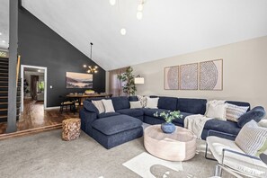 Una sala de estar moderna con un sofá modular, una mesa redonda de centro y un comedor con mesa y sillas.