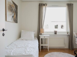 A bedroom with a single bed, a bedside table, a window with curtains, a radiator, and a small potted plant. - 6 Person Holiday Home in Tyresjo (Tyreso)