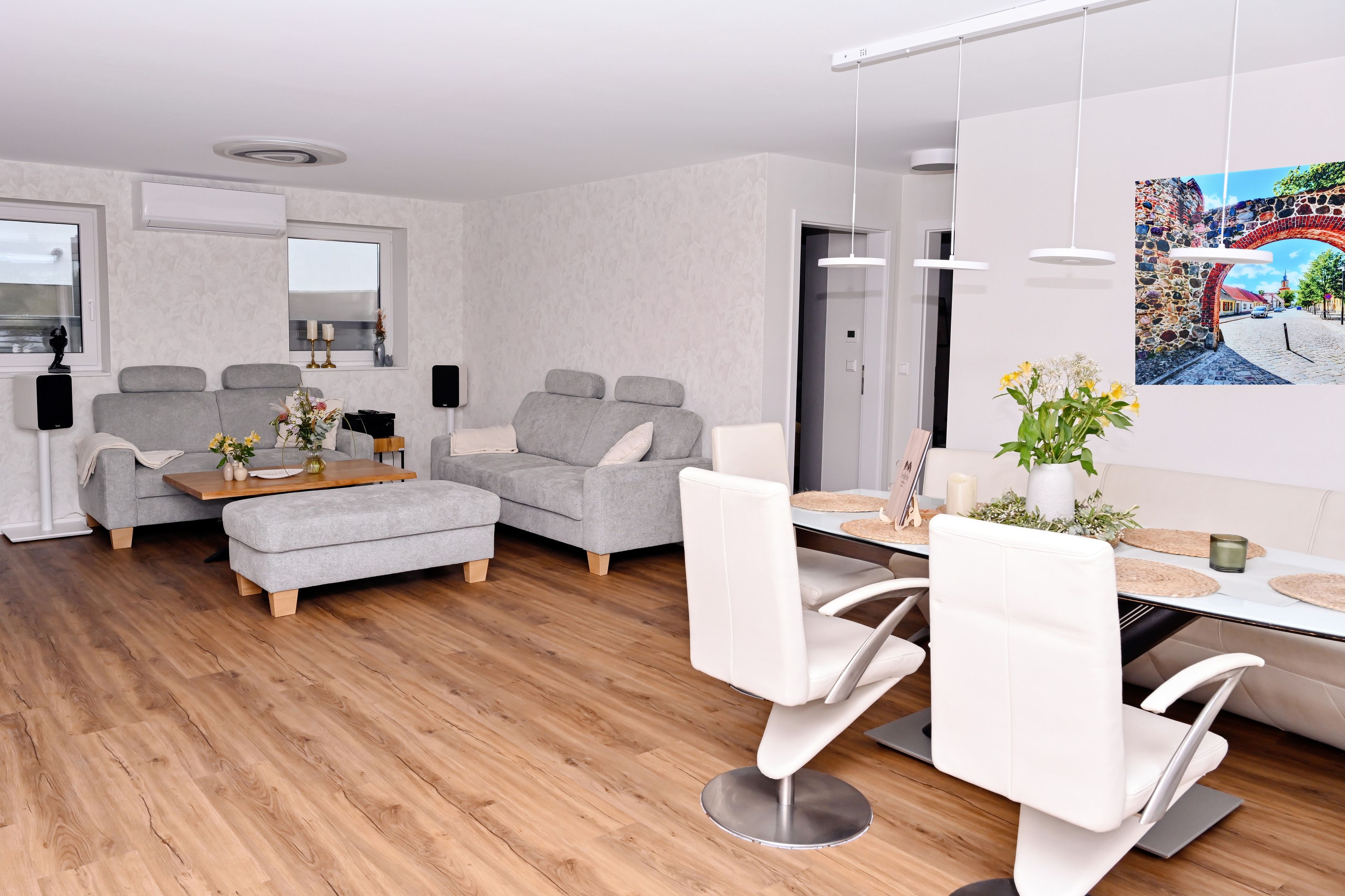 Ein modernes Wohnzimmer mit einem grauen Sofa, einem Holztisch und einem Essbereich mit weißen Stühlen und einem Tisch.