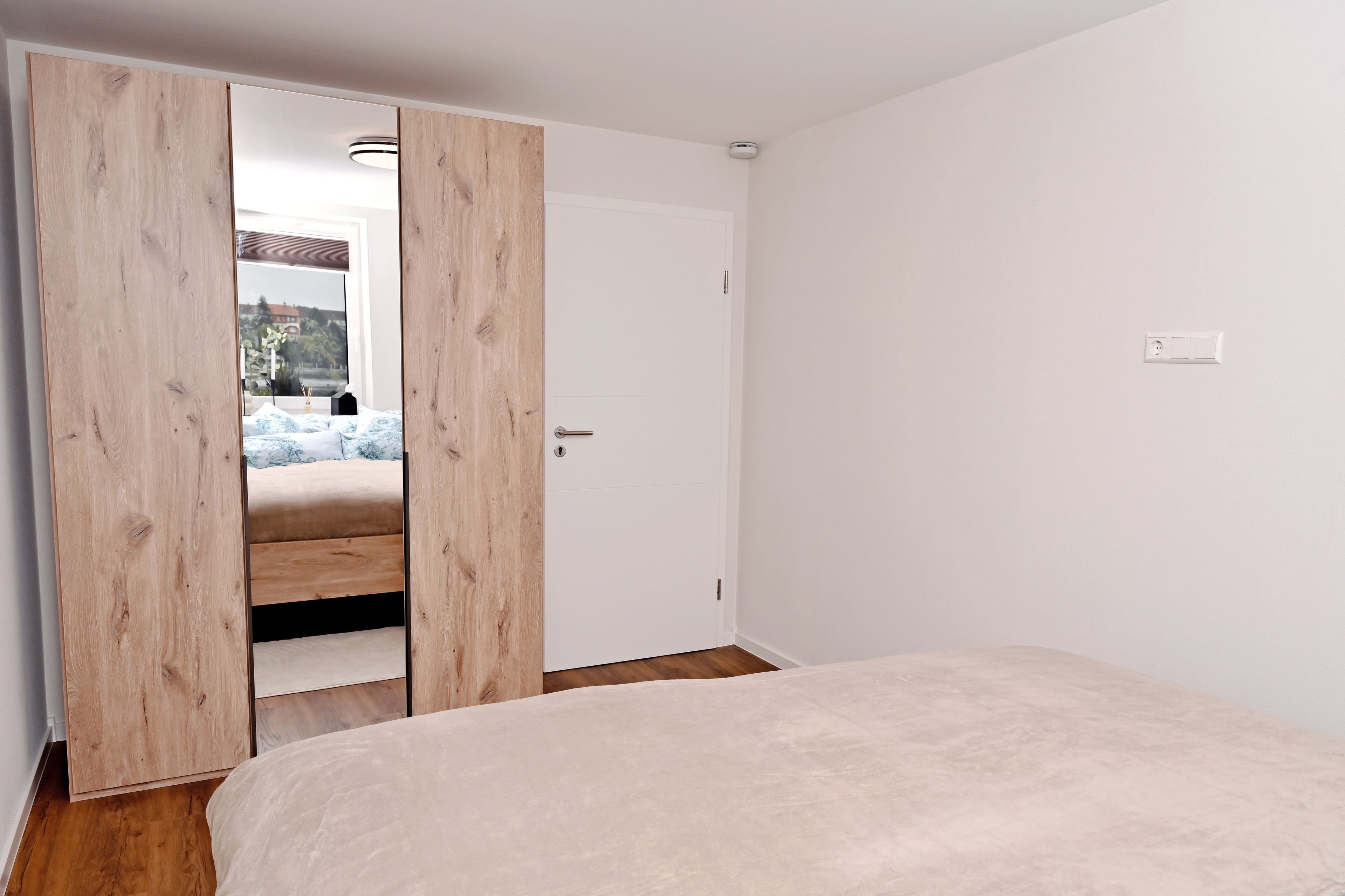 Een slaapkamer met een bed, een houten garderobe en een witte deur.