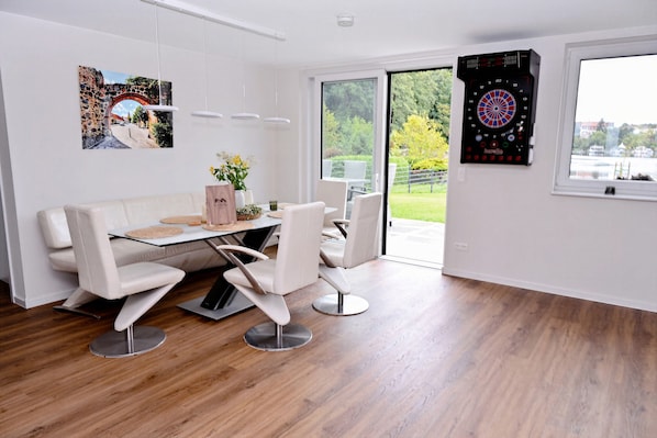 A modern dining area with a glass table, white chairs, and a dartboard.