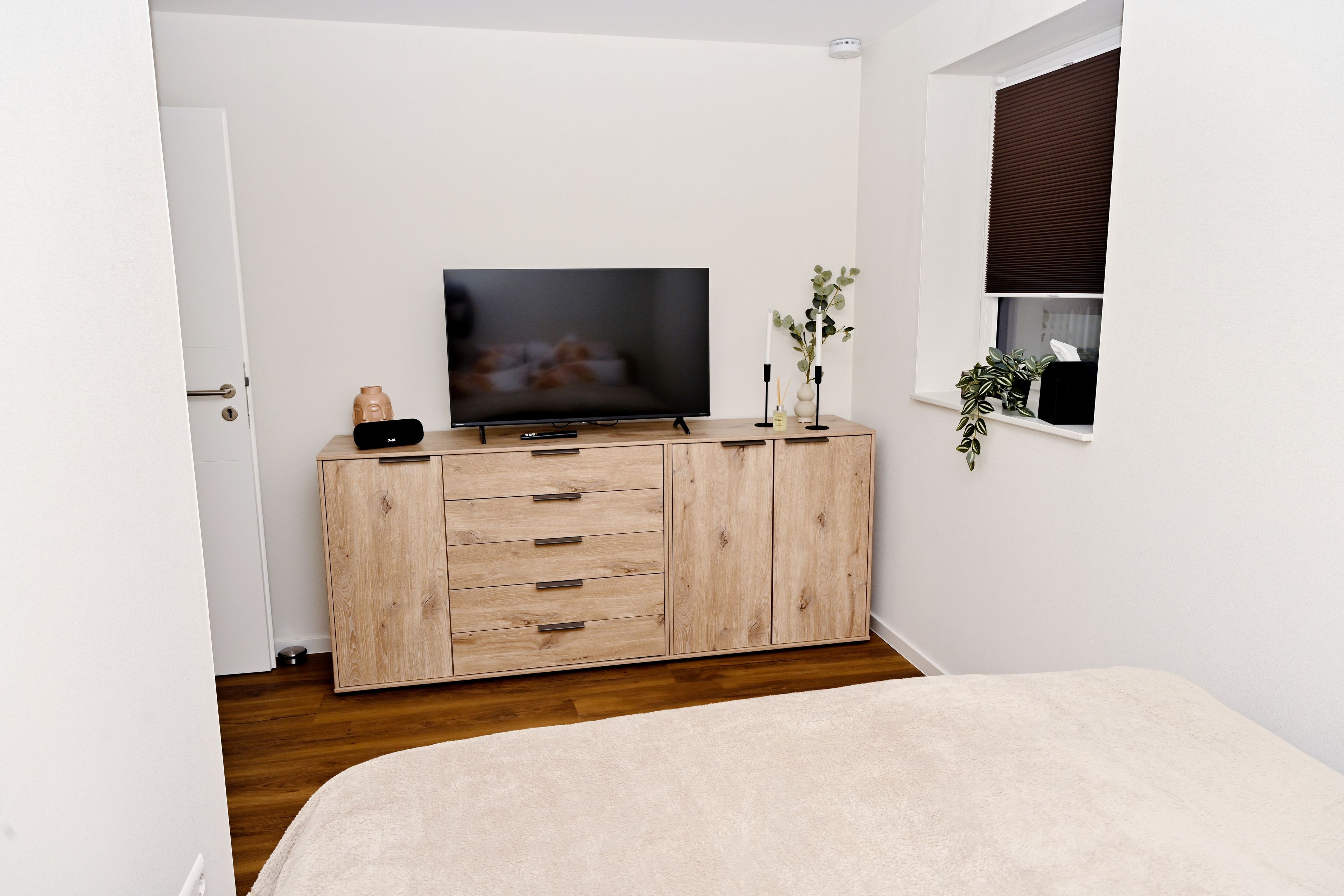 A bedroom with a wooden cabinet, a television, and a window with blinds.