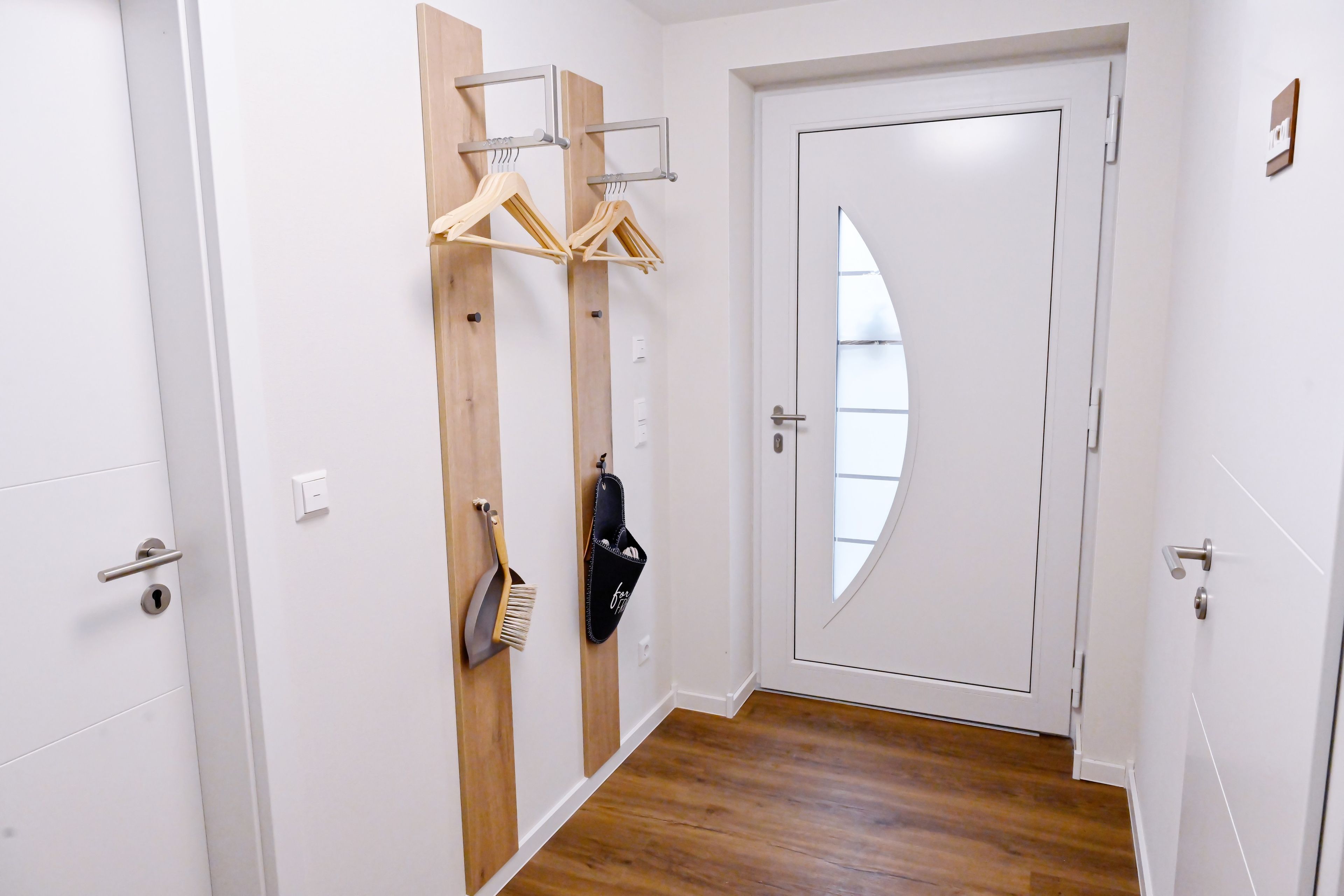 A hallway with a white door, wooden paneling, a broom, and a hanging garment rack.