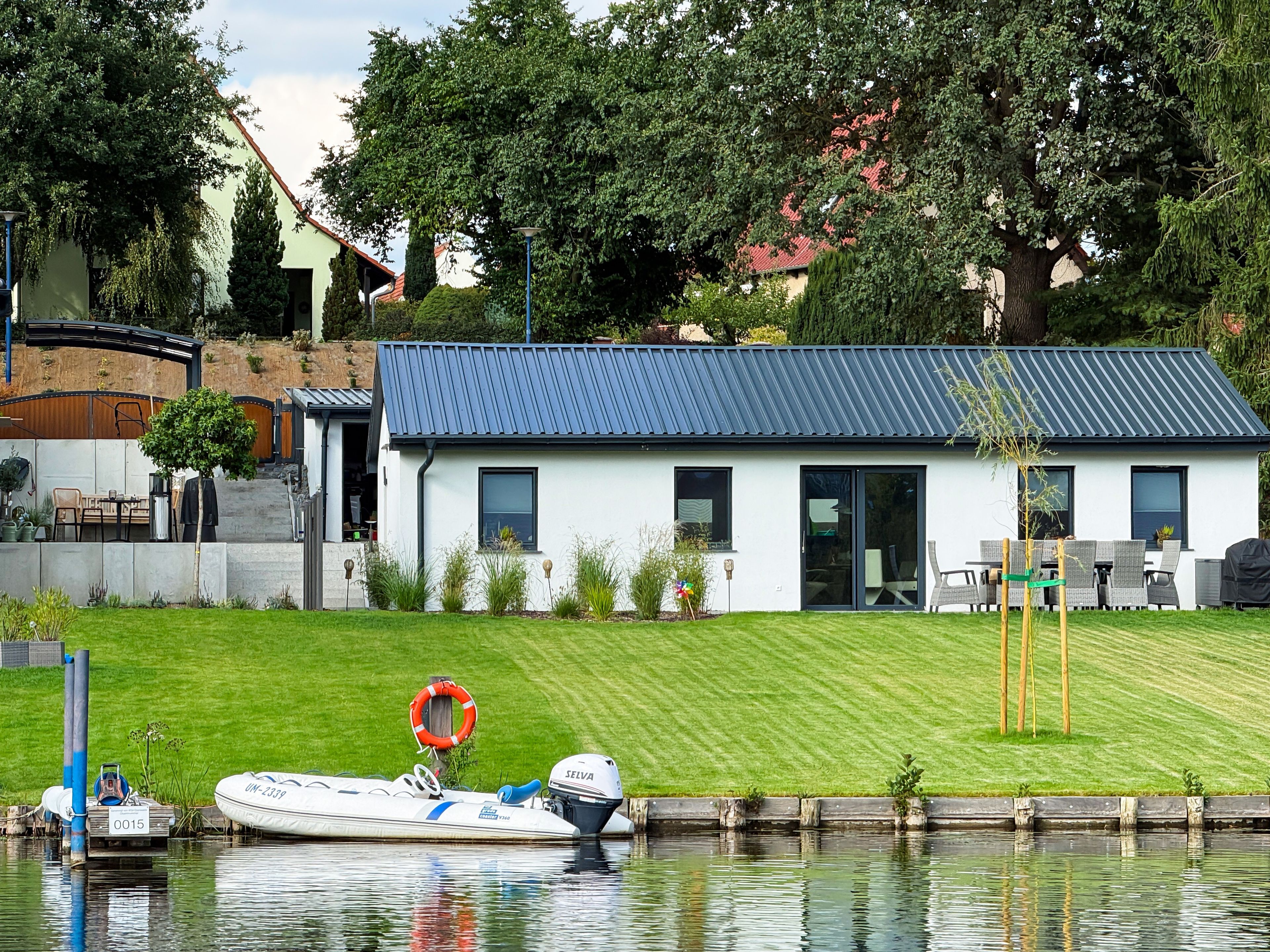 Ein Haus mit blauem Dach, einer grünen Wiese und einem Steg mit einem Boot.