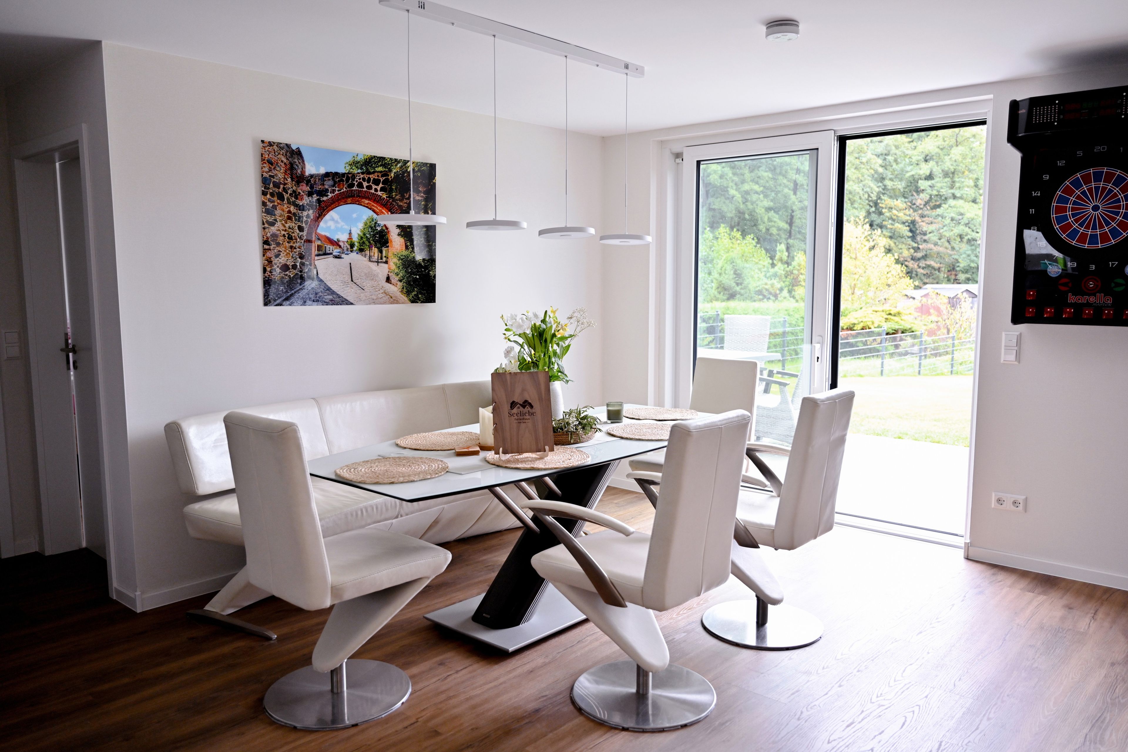 A modern dining area with a glass table, white chairs, and a white sofa.