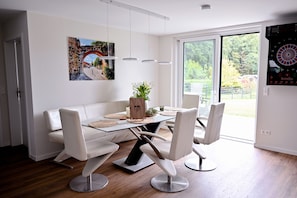 A modern dining area with a glass table, white chairs, and a white sofa.