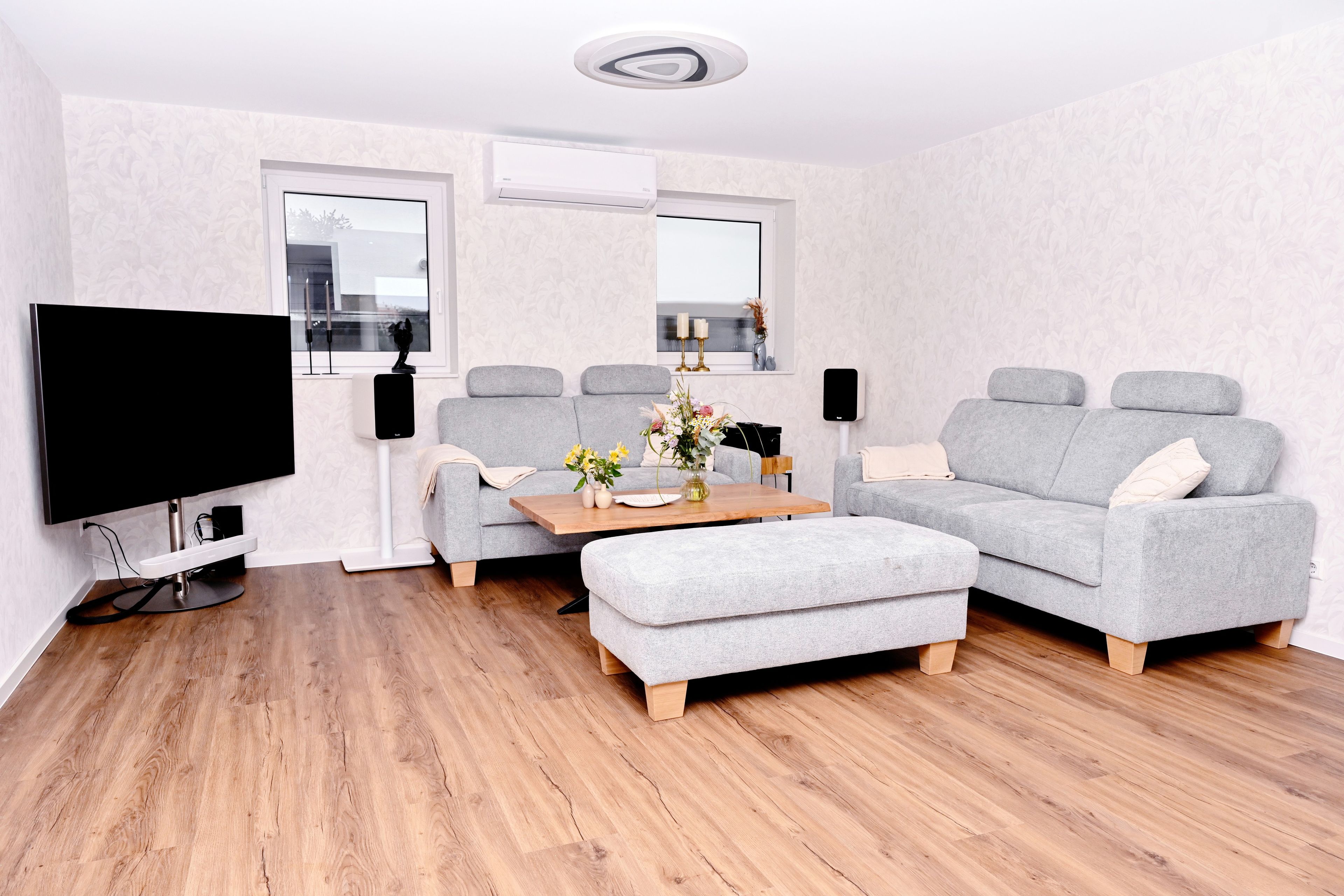 A modern living room with a grey sofa, a wooden coffee table, a flat-screen TV, and a ceiling light fixture.