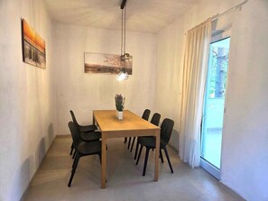 A dining area with a wooden table, black chairs, a hanging light fixture, and a window with curtains. - Holiday Apartment With Air Conditioning (Risika)
