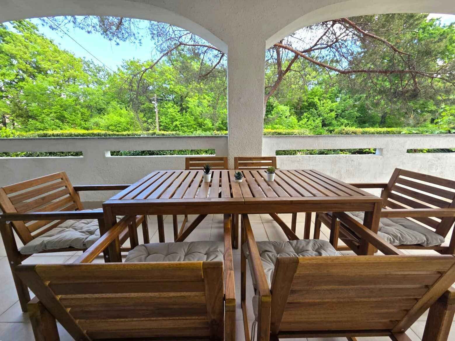 Un conjunto de mesa y sillas de madera en un patio con vista a árboles verdes.