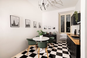 A modern kitchen with a checkered floor, a dining area with green chairs, and framed cityscape pictures on the wall. - Bright and spacious apartment in Rome's Ostiense and Gazometro neighborhoods (Roma)