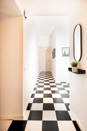 A hallway with a checkered floor, a door at the end, and a wall-mounted mirror. - Bright and spacious apartment in Rome's Ostiense and Gazometro neighborhoods (Roma)