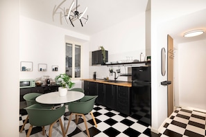 A modern kitchen with a black and white checkered floor, a dining area with two green chairs, and a unique ceiling light fixture. - Bright and spacious apartment in Rome's Ostiense and Gazometro neighborhoods (Roma)