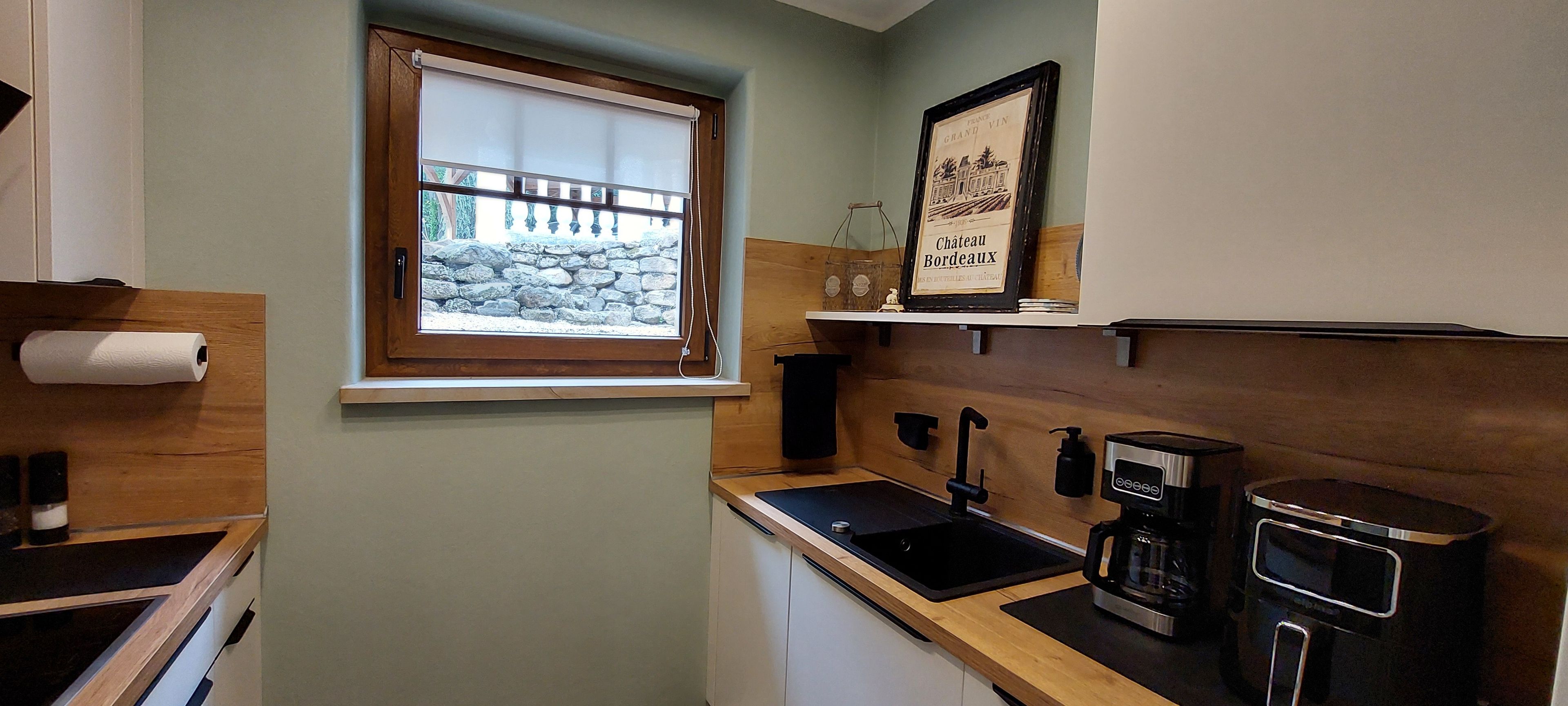 A small kitchenette with a window, a coffee maker, and a framed picture on the wall.