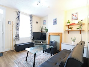 A living room with a sofa, a glass-top coffee table, a flat-screen TV, a fireplace, and a plant shelf. - Dover Retreat (Ipswich)