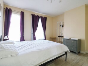 A bedroom with a bed, a wardrobe, a shoe rack, and a window with curtains. - Dover Retreat (Ipswich)