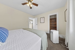 A bedroom with a bed, a ceiling fan, a white heater, and a door leading to another room. - Midtown Mobile Gem Near Downtown (Mobile)