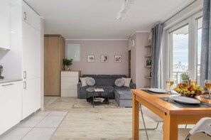 Ein gemütlicher Wohnraum mit Küchenzeile, einer grauen Sofagarnitur, einem Esstisch mit Stühlen und Blick auf die Stadt durch große Fenster.