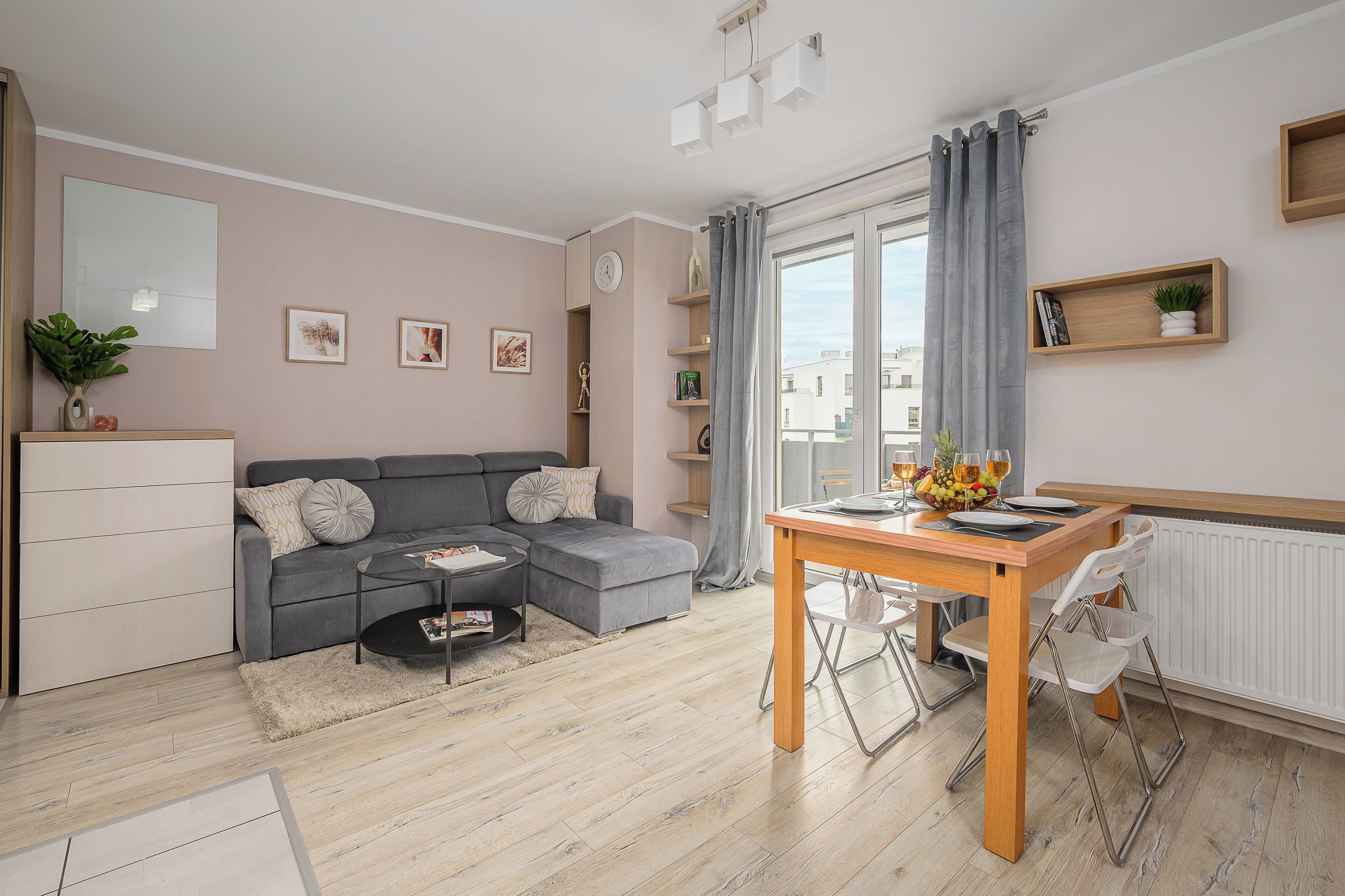 Una sala moderna con un sofá gris, una mesa de centro y una zona de comedor con una mesa de madera y sillas.