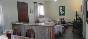 A living area with a dining table, chairs, a sofa, a TV, and a potted plant. - Address 442 (Águas de São Pedro)