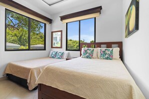 A bedroom with two beds, large windows, and a view of greenery. - Casa Serena | Spacious Comfort, Private Pool (Playas del Coco)