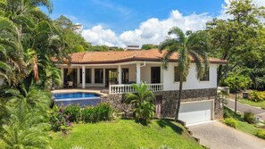 A two-story house with a swimming pool, surrounded by lush greenery and a clear sky. - Casa Serena | Spacious Comfort, Private Pool (Playas del Coco)