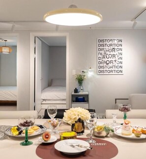 A hotel room with a dining table set for a meal, a bed, and a wall with a repeated word pattern. - Seoul Pause (Mapo-gu)
