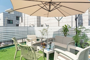 An outdoor seating area with wicker furniture, a table with condiments, and a large umbrella. - Seoul Pause (Mapo-gu)